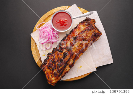 Grilled pork ribs with sliced onions and sauce on a wooden board Grilled pork ribs with sliced onions and sauce on a wooden board 139791393