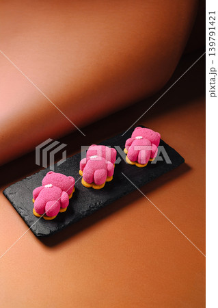 Three pink bear-shaped desserts on a black plate in a simple setting 139791421