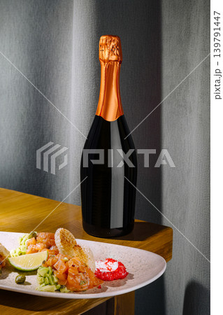 Champagne bottle next to salmon tartare dish with lime on wooden table 139791447