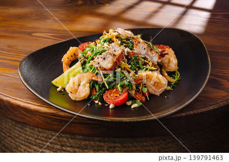 Shrimp salad with grilled fish served on a black plate in a restaurant 139791463