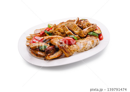 Grilled chicken, pork ribs, and vegetables served on a white plate at a dinner table Grilled chicken, pork ribs, and vegetables served on a white plate at a dinner table 139791474