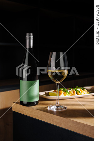 Wine bottle and glass next to a plate of food on wooden table in a bar 139791558