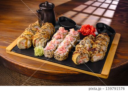 Sushi rolls arranged on a wooden platter with dipping sauce and garnishes Sushi rolls arranged on a wooden platter with dipping sauce and garnishes 139791576