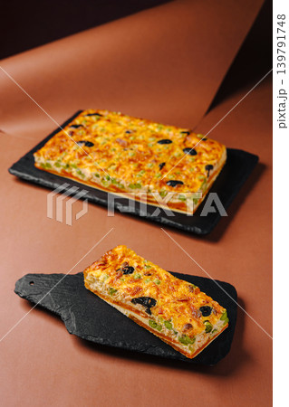 Baked dish with green vegetables and olives sits on black trays on table Baked dish with green vegetables and olives sits on black trays on table 139791748