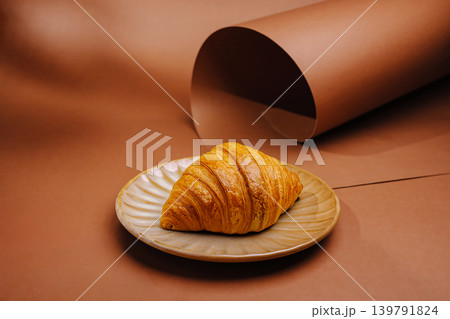 Fresh croissant on a plate with brown background and rolled paper Fresh croissant on a plate with brown background and rolled paper 139791824