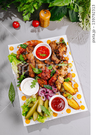 Delicious grilled meat platter served with sauces and vegetables on a table Delicious grilled meat platter served with sauces and vegetables on a table 139792313