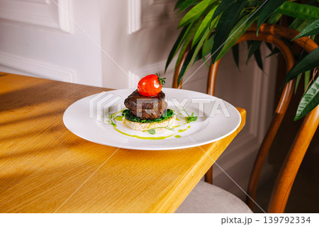 Beef tenderloin steak on crouton with cherry tomato served on white plate with fresh ingredients at restaurant 139792334