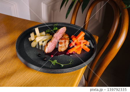 Duck dish served with vegetables on a black plate in a cozy setting 139792335