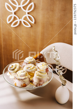 Fresh cinnamon rolls with icing on a glass plate in a cozy room setting Fresh cinnamon rolls with icing on a glass plate in a cozy room setting 139792375