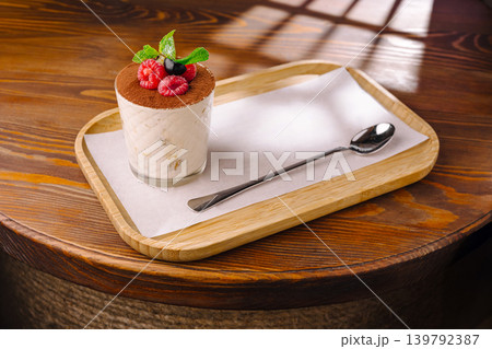 Tiramisu dessert with raspberries in glass on tray at a dining table in a cafe Tiramisu dessert with raspberries in glass on tray at a dining table in a cafe 139792387