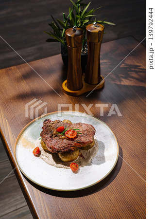 Steak with potatoes and cherry tomatoes on a wooden table in a restaurant Steak with potatoes and cherry tomatoes on a wooden table in a restaurant 139792444