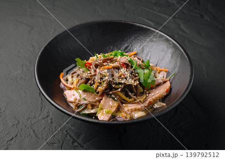 Noodle dish with sliced meat and vegetables served in a black bowl 139792512
