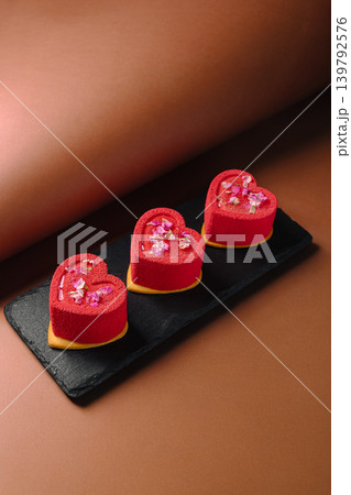 Three red heart-shaped desserts on a black plate Three red heart-shaped desserts on a black plate 139792576
