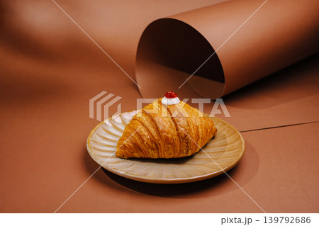 Croissant with cherry on top served on a plate with brown background Croissant with cherry on top served on a plate with brown background 139792686