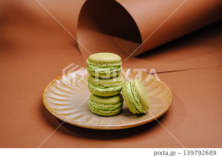 Green macarons stacked on a plate with brown background and paper roll Green macarons stacked on a plate with brown background and paper roll 139792689