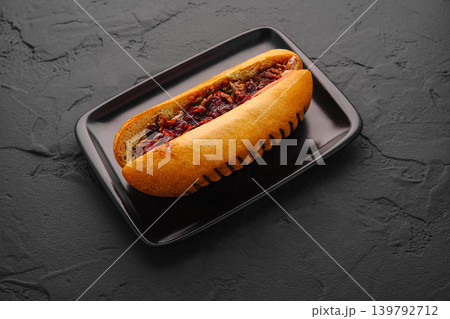 Hot dog served on a black plate with toppings and seasoning Hot dog served on a black plate with toppings and seasoning 139792712