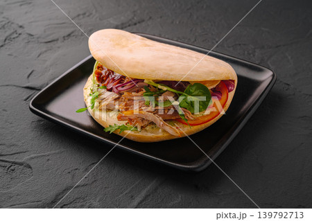 Sandwich with meat, vegetables, and sauce on a black plate in a kitchen setting Sandwich with meat, vegetables, and sauce on a black plate in a kitchen setting 139792713