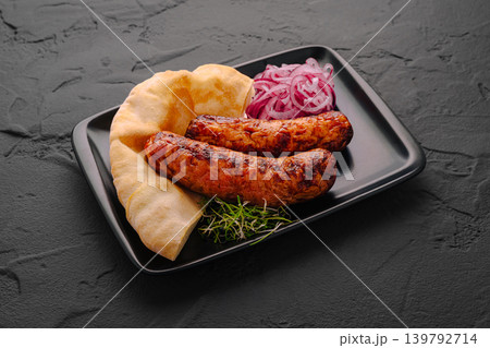 Sausages with flatbread and onions on a black plate in a kitchen setting Sausages with flatbread and onions on a black plate in a kitchen setting 139792714