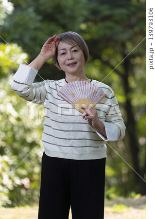 新緑の公園で扇子で扇いで涼むシニア女性 新緑の公園で扇子で扇いで涼むシニア女性 139793106