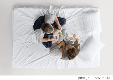 Couple sitting on white bed from overhead view and drinking coffee together. Couple sitting on white bed from overhead view and drinking coffee together. 139794818