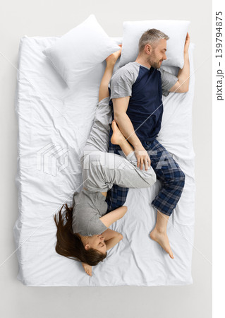 Couple sleeping in upside down pose on white bed from overhead view Couple sleeping in upside down pose on white bed from overhead view 139794875