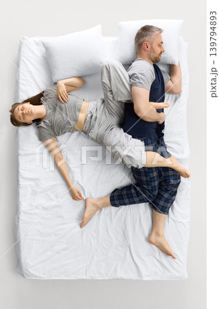 Couple sleeping in tangled pose on white bed from overhead view. 139794893