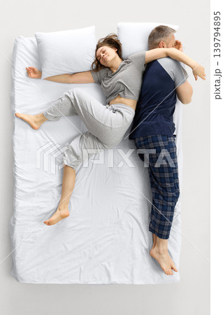 Woman stretching across white bed while man sleeps back to back. Woman stretching across white bed while man sleeps back to back. 139794895