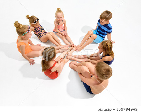 Children sitting in circle with feet together on white studio floor. Children sitting in circle with feet together on white studio floor. 139794949