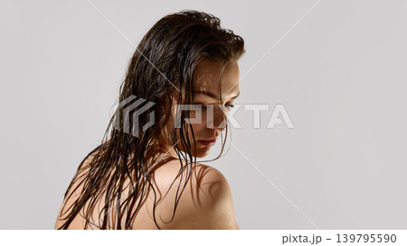 Calm woman with wet brunette hair looking down in minimal beauty studio Calm woman with wet brunette hair looking down in minimal beauty studio 139795590