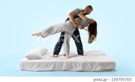 Man dipping woman backward on white bed from side view against blue background. 139795703
