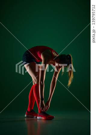Female athlete bending forward in post run stretch on green studio background Female athlete bending forward in post run stretch on green studio background 139795712