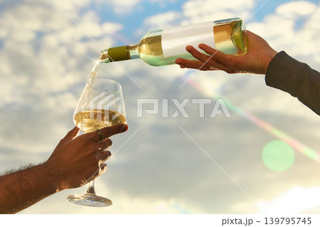 White wine pouring into glass against bright sky with sun flare 139795745