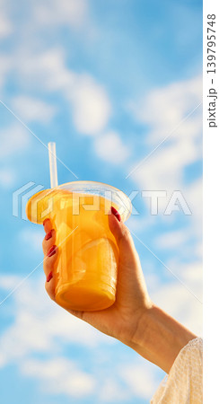 Orange iced drink in takeaway cup with blue sky copy space. 139795748