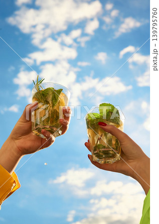 Two sparkling mint cocktails raised against blue sky. Two sparkling mint cocktails raised against blue sky. 139795760