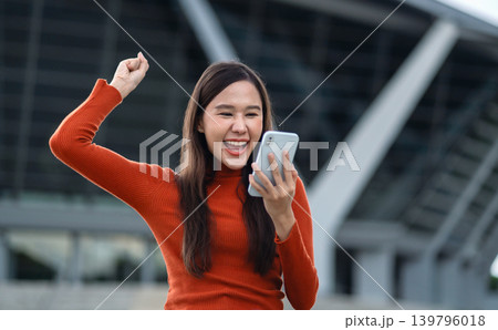 Young woman celebrates joyfully while holding smartphone 139796018