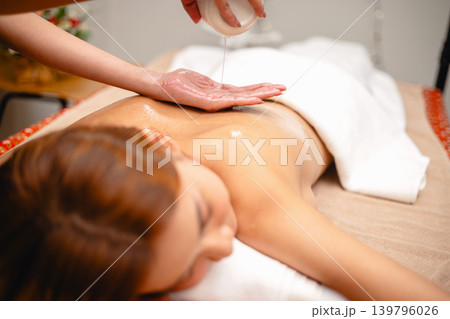 Woman relaxes with oil being poured gently over her skin 139796026
