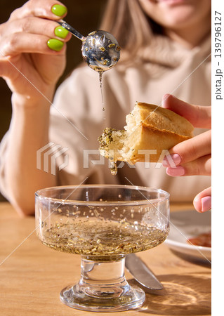 Hand pouring herb oil over bread above glass bowl in appetizing closeup. Hand pouring herb oil over bread above glass bowl in appetizing closeup. 139796127