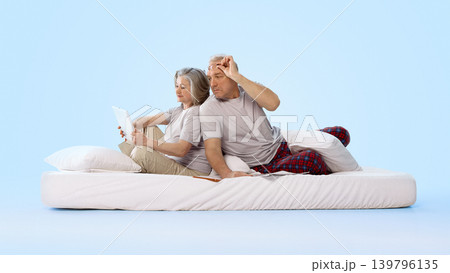 Older couple using tablet and reading newspaper on bed in clean studio scene. 139796135