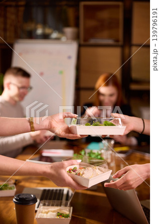 Hands passing lunch boxes across office meeting table. 139796191