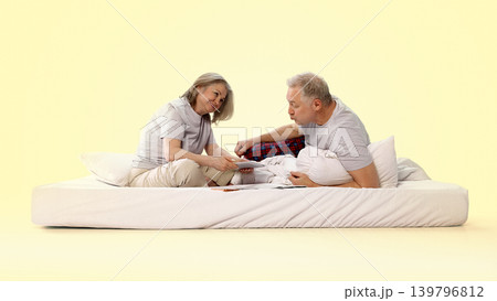 Senior couple sitting on bed and using tablet in minimalist bedroom setup Senior couple sitting on bed and using tablet in minimalist bedroom setup 139796812