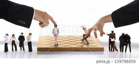 Giant hands moving miniature people on chess board with spectators. 139796859