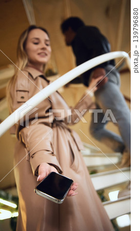 Woman holding smartphone on stairs with blurred man in background. Woman holding smartphone on stairs with blurred man in background. 139796880
