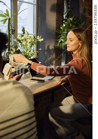 Woman making payment with smartwatch near laptop and handbag in stylish workspace Woman making payment with smartwatch near laptop and handbag in stylish workspace 139796886