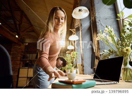 Woman reaching for smartphone for mobile banking near laptop in creative workspace Woman reaching for smartphone for mobile banking near laptop in creative workspace 139796895