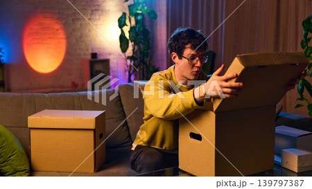 Young man opening delivery box at home unboxing online order ecommerce experience 139797387