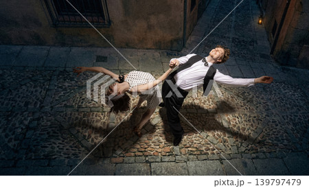 Lindy hop couple performing dip on cobblestone street at night under spotlight vintage energy 139797479
