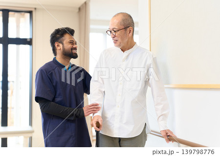 手すりと杖を使って歩く練習をするシニアと外国人介護士 手すりと杖を使って歩く練習をするシニアと外国人介護士 139798776