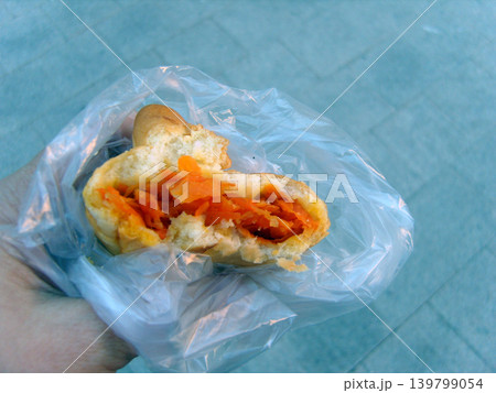 Fresh baked pastry with carrot filling held in hand inside a transparent plastic bag. Simple street food snack with soft bread texture and bright orange vegetable stuffing on a blurred background Fresh baked pastry with carrot filling held in hand inside a transparent plastic bag. Simple street food snack with soft bread texture and bright orange vegetable stuffing on a blurred background 139799054