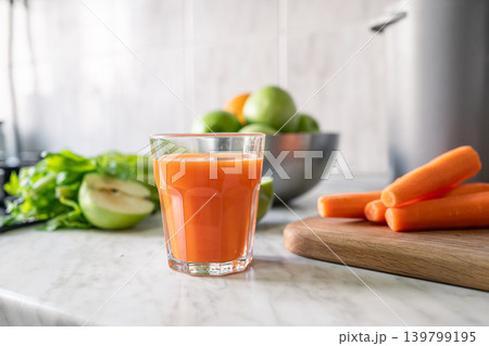 Fresh carrot juice in glass with celery and green apples on kitchen table Fresh carrot juice in glass with celery and green apples on kitchen table 139799195