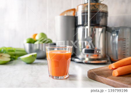 Fresh carrot juice near juicer with apples and vegetables in kitchen 139799196